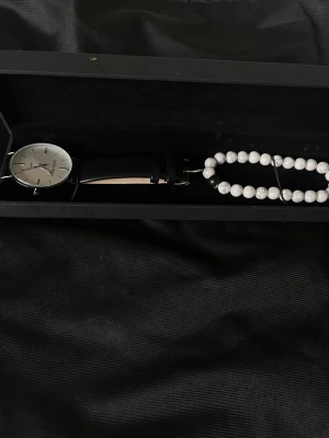 Daniel Philip klocka med svart läderband - Stilren klocka från Daniel Philip med silverfärgat ur och svart läderband. Urtavlan är enkel och elegant med minimalistiska markeringar. Kommer i originalask tillsammans med ett vitt pärlarmband.