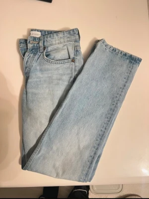 Ljusblå raka jeans från Zara - Säljer ett par ljusblå jeans från Zara med rak passform och klassisk femficksdesign. Jeansen har knäppning med knappar framtill och är tillverkade i bomull. Dem är lite slitna se bild.