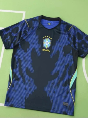 Blå Brasil fotbollströja CBF - Snygg blå fotbollströja från Brasilien med CBF-logga och gula detaljer. Tröjan har ett unikt mönster i svart och blått, rund halsringning och korta ärmar. Perfekt för träning eller match. Tillverkad i lätt och ventilerande material.