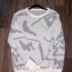 Vit och grå stickad tröja - Säljer en oversized stickad tröja i vitt med ljusgrått abstrakt mönster. Tröjan har rund halsringning, långa ärmar och ribbade muddar vid ärmslut och nederkant. Perfekt för dig som gillar en avslappnad och trendig stil.