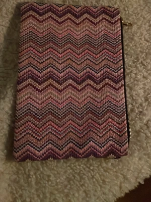 Zigzag-mönstrad datafodral - Säljer ett datafodral med ikoniskt zigzag-mönster i olika nyanser av rosa, lila och beige. Väskan har en rektangulär form och stängs med dragkedja i guld. Perfekt accessoar för att lyfta din outfit med lite färg och mönster.