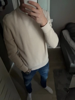 Beige strukturerad sweatshirt från Zara - Säljer en stilren beige sweatshirt med rund hals och diskret struktur i materialet. Tröjan har långa ärmar och en avslappnad passform, perfekt att matcha med jeans för en clean look.