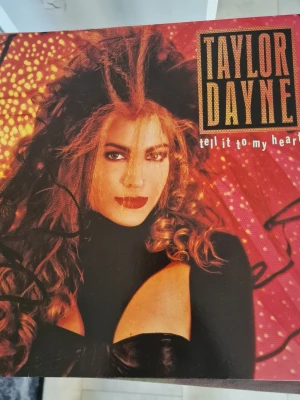 Taylor Dayne Tell It To My Heart LP - Vinylskiva med Taylor Daynes album 'Tell It To My Heart'. Omslaget har starka färger i rött, orange och svart med artistens namn och albumtitel tydligt tryckt. Baksidan visar låtlista och svartvit bild på artisten. Perfekt för dig som gillar 80-talsmusik och samlar på LP-skivor. Inga repor.