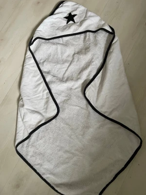 Vit mjuk frotté bad handduk med svart kant - En vit, mjuk frottéhandduk eller sovplagg med svart kant och en svart stjärna i ena hörnet. Perfekt för att mysa hemma eller använda som loungewear. Materialet känns som frotté och är skönt mot huden.efter bad 