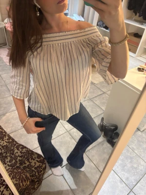 Randig offshoulder topp  - Säljer en söt offshoulder topp med blå och vita ränder. Toppen har trekvartsärm och en lös passform som ger en chill vibe. Tillverkad i mjuk bomull, perfekt för varmare dagar. Passar till både jeans och kjol för en trendig look.