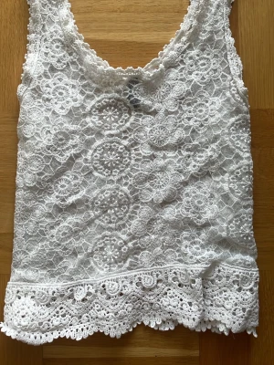 Vit spetslinne 🤍 - Supersött vitt spetslinne med blommigt mönster och bred spetskant nedtill🤍! Linnet är ärmlöst och har rundad halsringning. Toppen är perfekt till att ha under en tjocktröja.
