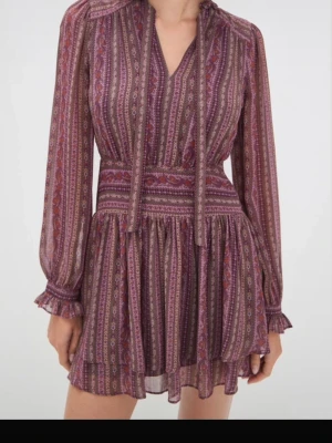 Mönstrad kortklänning med volang - Kortklänning i lila och vinröda toner med långärmade, transparenta ärmar och volangkant. Så snygg designer klänning från Paige. Helt ny med prislapp. Så cool med mönster. Nypris är ca 4000 kr. Säljer då den inte passar eller används. 