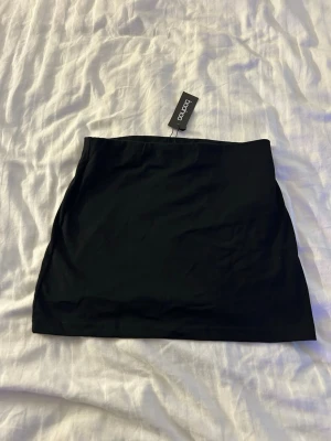 Svart minikjol från Boohoo - En enkel och stilren svart minikjol från Boohoo. Kjolen har en tight passform och är gjord i ett mjukt och stretchigt material som sitter snyggt på kroppen. Perfekt att matcha med en crop top eller oversized tröja för en trendig look.