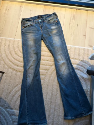 Blå True Religion Joey flare jeans - True religion jeans, low wais och bootcut. Har super fin tvätt och fina sömmar som detaljer på jeansen. Använd fåtal gånger. 