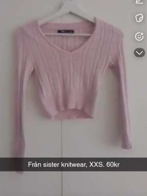 Ljusrosa cropped stickad tröja - Supersöt ljusrosa stickad tröja från Sister Knitwear med V-ringning och ribbade detaljer. Croppad modell med långa ärmar och diskret kabelstickat mönster. Perfekt för lager på lager och en chill look.