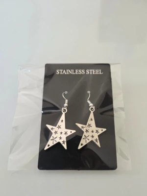 Stjärnformade örhängen i stål - Snygga örhängen i rostfritt stål med stjärnformad design och små utskurna stjärnor i varje hänge. Silverfärgade och lätta att matcha med olika stilar. Perfekta för dig som gillar unika accessoarer med lite edge.