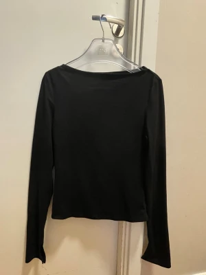 Svart långärmad topp med slits - En svart långärmad topp med slits vid ärmsluten. Enkel och stilren design med rak passform och rund halsringning. Perfekt att styla till olika outfits för en clean look.