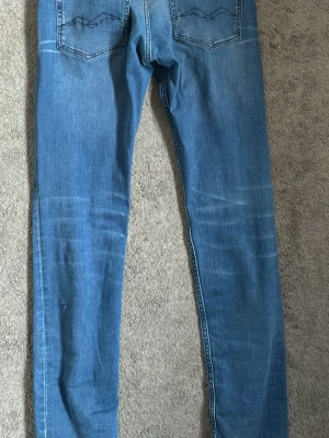 Blå slim fit jeans från Replay - Säljer ett par blå slim fit jeans från Replay med klassisk femficksmodell och snygga slitningar på framsidan. Jeansen har normal midja, dragkedjegylf och är tillverkade i stretchigt denimtyg för extra komfort. Använda ett fåtal gånger nästan som helt nya i kvaliten. Hör gärna av dig vid frågor.