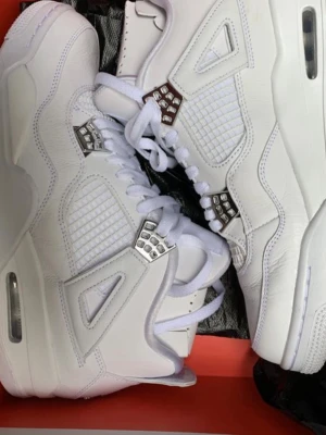 Vita Air Jordan 4 Retro sneakers - Säljer ett par helvita Air Jordan 4 Retro sneakers med detaljer i silver på snörningen. Skorna har en chunky sula, meshpaneler på sidorna och är tillverkade i läder. Klassisk siluett med ikoniska detaljer och bekväm passform.