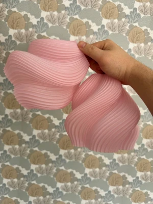 Rosa vågig lampskärm i plast - Unik rosa lampskärm med vågigt, ribbat mönster och modern design. Tillverkad i plast och passar perfekt för att ge rummet en cool och kreativ touch. Skärmen har ett hål upptill för montering på lampa eller sladd. Det är passning för E14 sockel. 