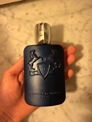 Parfums de Marly BYTER! - Exklusiv parfym från Parfums de Marly i en matt mörkblå flaska med silverfärgat lock. Flaskan har ett elegant reliefmönster med två hästar och texten '1743' samt 'PARFUMS DE MARLY PARIS'. Lyxig och stilren design som sticker ut i badrumshyllan.