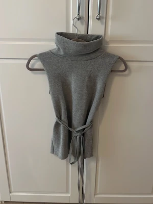 Stickat Polo linne från Zara - Ett grått stickat polo linne från Zara med knyt i midjan(bandet går och ta av samt har öglor för bandet) som är nästan oanvänt och i bra skick.