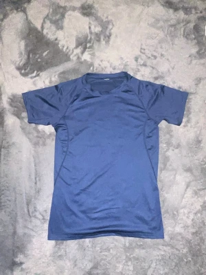  Blå kompression T-shirt - En enkel och stilren blå t-shirt med korta ärmar och rund hals. Tillverkad i ett lätt och stretchigt syntetmaterial som passar perfekt för träning eller en aktiv vardag. T-shirten har en smal passform och är helt utan mönster eller tryck. Inga lappar heller