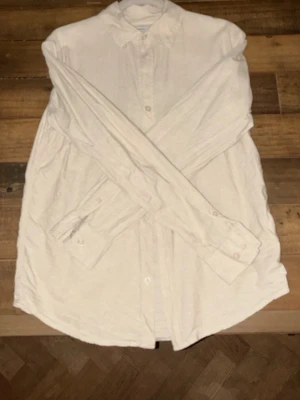 Beige linneskjorta med knappar - Stilren beige skjorta i linne med klassisk krage och knäppning framtill. Skjortan har långa ärmar med manschetter och en avslappnad passform. Perfekt för en enkel och clean look.