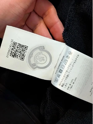 Svart ziptröja från Moncler - Svart ziptröja från Moncler med hög krage och logga på bröstet. Tröjan har dragkedja framtill, fickor med knapp och en snygg röd, vit och blå rand längs ena ärmen. Tillverkad i 100% bomull för en skön och sportig känsla.