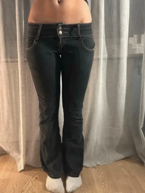 Vintage lågmidjade jeans - Snygga mörkgrå/svarta bootcut jeans med kontrasterande vita sömmar och dubbla knappar i midjan. Jeansen har låg midja, fram- och bakfickor samt utsvängda ben. Perfekta för dig som gillar en retro och avslappnad stil.