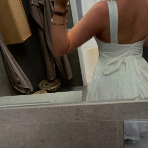 Vit omlottklänning med v-ringning - Säljer en vit klänning med breda axelband, v-ringad hals och rosettdetalj i ryggen🎀 Kjolen är lätt utställd och klänningen har en elegant, luftig känsla. Perfekt för student eller skolavslutning💗🌸