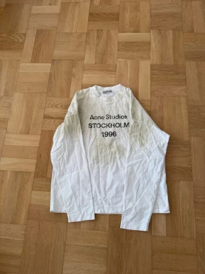 Vit långärmad t-shirt Acne Studios - Vit långärmad t-shirt från Acne Studios med svart text 'STOCKHOLM 1996' på bröstet. Klassisk rund halsringning och rak passform. Materialet är mjuk bomull och designen är enkel men trendig, perfekt för dig som gillar stilrena plagg med statement-tryck. Obs: inte säker på legit 