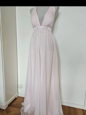 Ljusrosa långklänning med v-ringning - Buda gärna!! Säljer en elegant ljusrosa långklänning med djup v-ringning och markerad midja. Klänningen har ett flytande, svepande fall och är ärmlös. Perfekt för bal eller student. Materialet känns lätt 