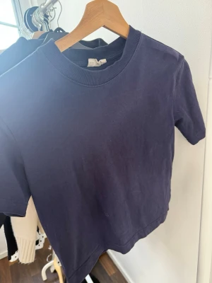Mörkblå t-shirt från Gina Tricot - En basic mörkblå t-shirt från Gina Tricot i modellen 'basically basic'. T-shirten har korta ärmar, rund halsringning med ribbad kant och är gjord i mjuk bomull. Perfekt till jeans eller kjol för en enkel och clean look.