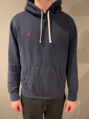 Marinblå Ralph Lauren hoodie - Säljer denna väldigt populära Ralph Lauren hoodie. Storlek L. Han på bild är 185cm, 77kg. Hoodien är äkta vilket man kan se när man scannar QR koden. Pris kan diskuteras vid snabb affär!