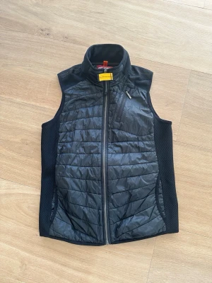 Svart dunväst från Parajumpers - Snygg svart dunväst från Parajumpers med quiltat mönster, hög krage och dragkedja framtill. Västen har meshpaneler på sidorna för extra ventilation och en bröstficka med dragkedja. Perfekt för lager-på-lager och streetstyle.