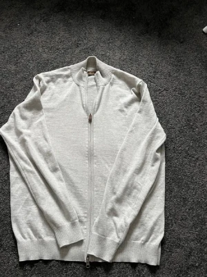 Ljusgrå ziptröja med ribbade muddar -  Stenström,Ljusgrå ziptröja,hel dragkedja framtill. Tröjan har ribbade muddar vid ärmslut och nederkant, samt en enkel och stilren design.  Storlek XL men passar L och M.