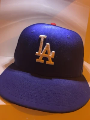 Blå LA-keps från New Era storlek 6 7/8 - Snygg blå keps från New Era med LA-logga broderad i vitt framtill och en liten röd detalj på toppen. Inte jätte använd bra skick.