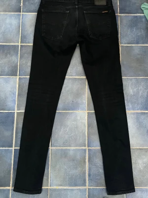 Mörkblå nudie jeans - Säljer ett par mörkblå jeans från Nudie Jeans med klassisk femficksdesign och diskret broderi på bakfickorna. Jeansen har en perfekt passform och är tillverkade i mjuk denim med stretch för extra komfort. Perfekta för en clean och stilren look.