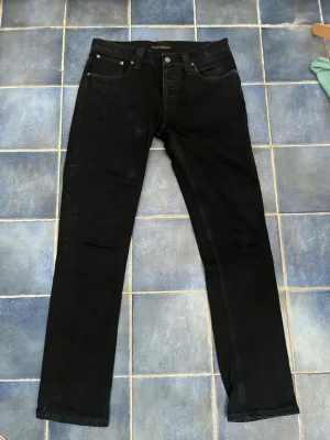 Svarta Nudie Jeans - Snygga svarta jeans från Nudie Jeans med klassisk femficksmodell och raka ben. Jeansen har diskreta sömmar och en stilren look, perfekta för dig som gillar en clean och enkel stil. Tillverkade i mjukt denimtyg som sitter skönt hela dagen.