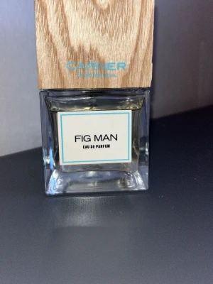 Carner Fig Man Eau de Parfum - Carner Fig Man Eau de Parfum i en stilren, fyrkantig glasflaska med trälock. Doften har en modern och fräsch känsla, och flaskan har en minimalistisk etikett med svart text och blå ram. Perfekt för dig som gillar exklusiva och unika parfymer. 90 ml kvar (Se på bild) 