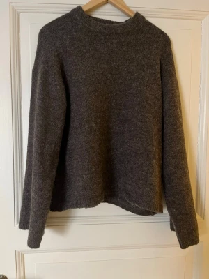 Mörkbrun stickad tröja Gina Tricot med sjal - Mysig mörkbrun stickad tröja från Gina Tricot i premiumkvalitet med tillhörande sjal. Tröjan har rund halsringning, långa ärmar och ribbstickade muddar vid hals, ärmslut och nederkant. Perfekt för kyliga dagar och enkel att matcha med olika outfits.