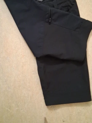 Svarta shorts från Everest med dragkedja - Svarta shorts från Everest med normal passform, tillverkade i slitstarkt syntetmaterial. Shortsen har dragkedjefickor fram och bälteshällor i midjan, perfekta för sommarens äventyr.