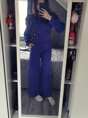 Lila set med byxor och tröja - Säljer en lila set med byxor och tröja med långa puffärmar och rund halsringning. Byxorna har en rak, lite vidare passform och plagget har en stilren look. Materialet känns mjukt och stretchigt, perfekt för dig som vill ha något bekvämt men ändå snyggt.