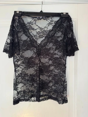 Svart spetsblus med v-ringning - Säljer en genomskinlig svart spetsblus från ZARA med v-ringad hals och korta ärmar. Blusen har ett blommigt spetsmönster och är perfekt för att styla lager på lager. 