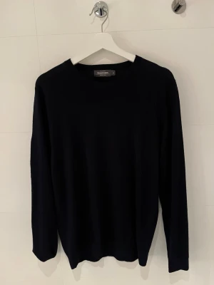 Svart merinoulltröja från Dressmann - Klassisk svart stickad tröja från Dressmann i mjuk merinoull. Tröjan har rund halsringning och långa ärmar, perfekt för lager på lager och enkel att matcha med olika stilar.