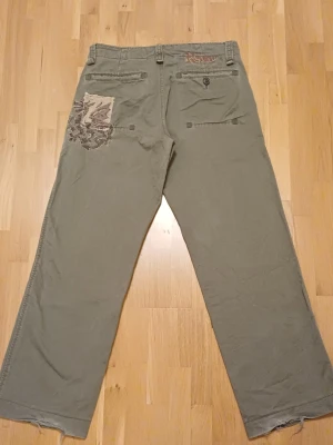 Replay byxor - As snygga och coola byxor med brodering och tryck av en drake och fin innerkant som man kan vika ned. Älskar men de kommer tyvärr inte till användning. Super bra kvalite och bortsätt från slitage i follarna så är de i gott skick. Midja 41cm - innerbenlängd 77cm - benvidd nedtill - 25cm - midjehöjd 24cm.