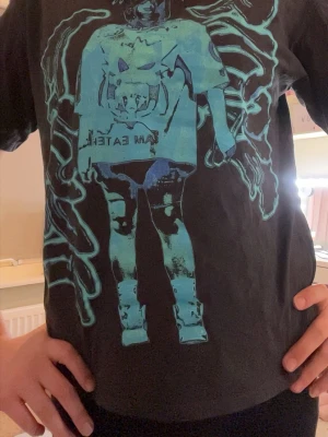 Svart Billie Eilish t-shirt  - Cool svart Billie Eilish t-shirt med ett stort blått grafiskt tryck av Billie Eilish och texten 'I AM EATER'. T-shirten har normal passform och korta ärmar. 