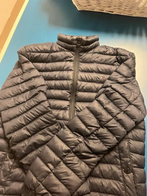  Tommy Hilfiger jacka - Snygg mörkblå dunjacka från Tommy Hilfiger med quiltad design och hög krage. Jackan har dragkedja framtill, sidofickor med knapp och diskret logga på bröstet. Insidan har ett randigt band i rött, vitt och blått. Perfekt för kalla vinterdagar.