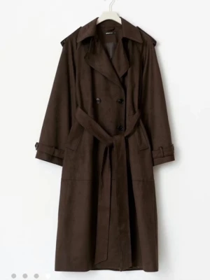 Mörkbrun trenchcoat med knytskärp - Stilren mörkbrun trenchcoat i mjukt material med klassisk dubbelknäppning, bred krage och knytskärp i midjan. Jackan har axelklaffar, fickor och justerbara band vid ärmsluten för extra detaljerad look. Endast använd en gång, från Gina tricot i storlek S💕