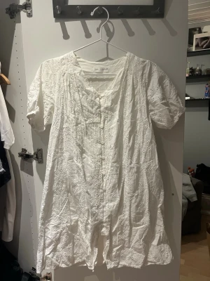 Vit broderad kort klänning från ZARA - Söt vit kort klänning från ZARA med broderade detaljer och v-ringning. Klänningen har korta ärmar, knappar framtill och ett luftigt, avslappnat fall. Perfekt för varma sommardagar, skolavslutning och student.