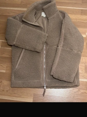 Beige-Brun  teddyjacka/fleecejacka- mysig och trendig - Superfin teddyjacka i en varm beige/ljusbrun nyans. Jackan är i ett mjukt, fluffigt material som ger en mysig och stilren look, den är perfekt för höst, nu i vår eller svalare sommarkvällar.  Den är i storlek Xs då den är oversized med hög krage och dragkedja framtill. Jackan är i väldigt bra skick, och har en sminkfläck på insidan av kragen, därav är det inget som märks eller syns när jackan bärs! 