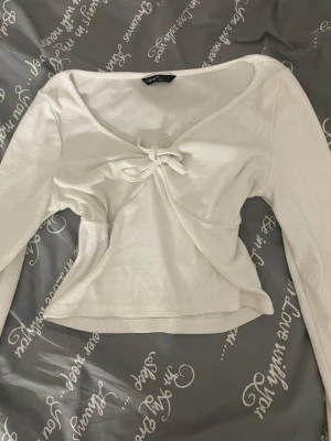 Vit ribbad topp med knyt  - Supersöt vit ribbad topp från SHEIN med lång ärm och snygg knytning framtill. Toppen har en lätt croppad passform och djupare ringning, perfekt att styla med jeans eller kjol. Materialet är mjukt och stretchigt för en bekväm känsla.