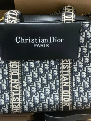 Christian Dior monogram handväska - Snygg handväska från Christian Dior med klassiskt blått och vitt monogrammönster och tydliga loggor. Väskan har svarta läderdetaljer, dragkedja i guld och breda axelband med Dior-tryck. Perfekt för dig som gillar lyxiga accessoarer och vill sticka ut.//fick den present