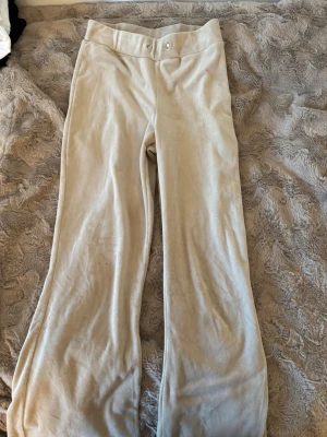 Beiga mjukisbyxor i velour - Säljer ett par beiga mjukisbyxor i mjuk velour med raka ben och bred linning. Byxorna har knappstängning framtill och är perfekta för chill dagar. Materialet är lent och ger en skön känsla. Passar dig som gillar en avslappnad och trendig stil.